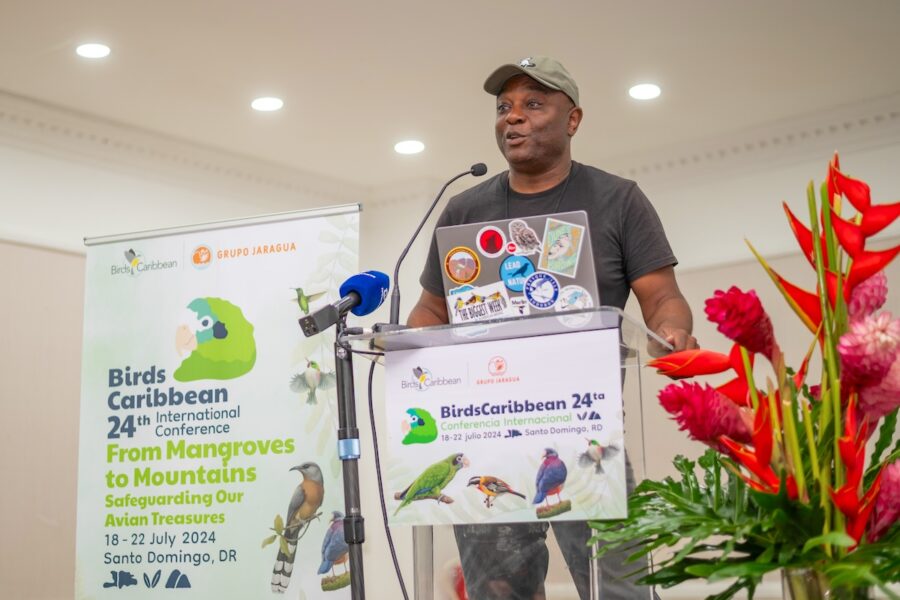 A man giving a keynote address on stage while standing behind a clear acrylic podium. 