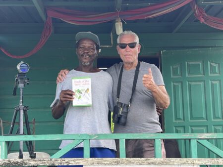 Bolt and Wayne stand in the hut at Woodbourne, whilst Bolt holds a Birds of the West Indies field guide.