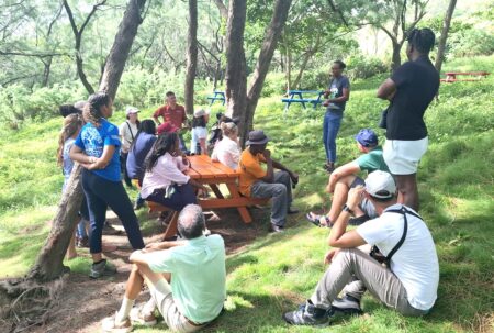 A women presenting to a group of people in the forest.